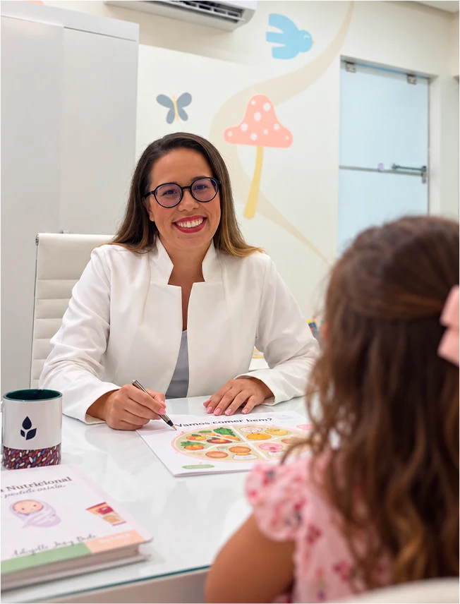 Dra. Adryelli Joicy Brito sorrindo com uma criança durante uma consulta nutricional